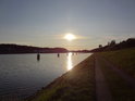 Klesající Slunce nad řadou kotevních kolíků v Nord-Ostsee-Kanal s cestou po západním břehu.